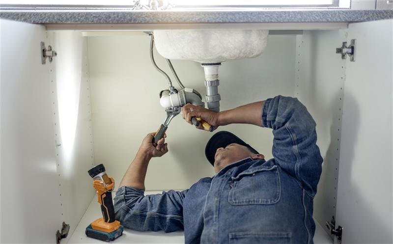 Plumber repairing pipes beneath a bathroom sink in Aurora