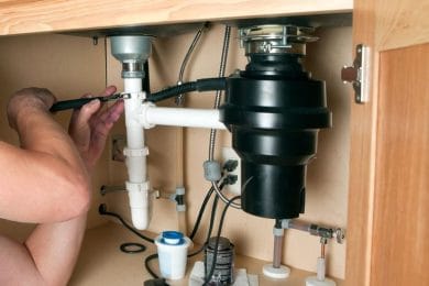 Plumber repairing a garbage disposal beneath a kitchen sink in Aurora