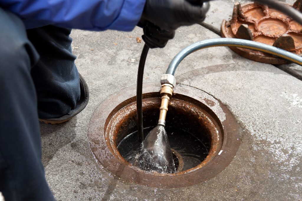 Plumber hydro jetting a sewer line through a manhole in Aurora