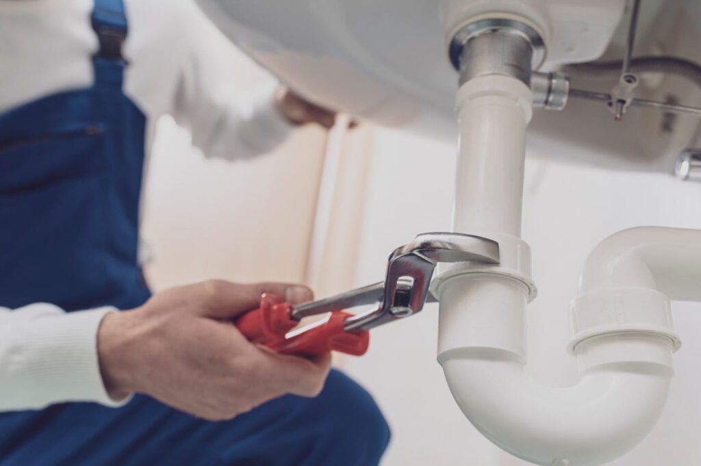Plumber repairing a white drain pipe beneath a sink in Aurora