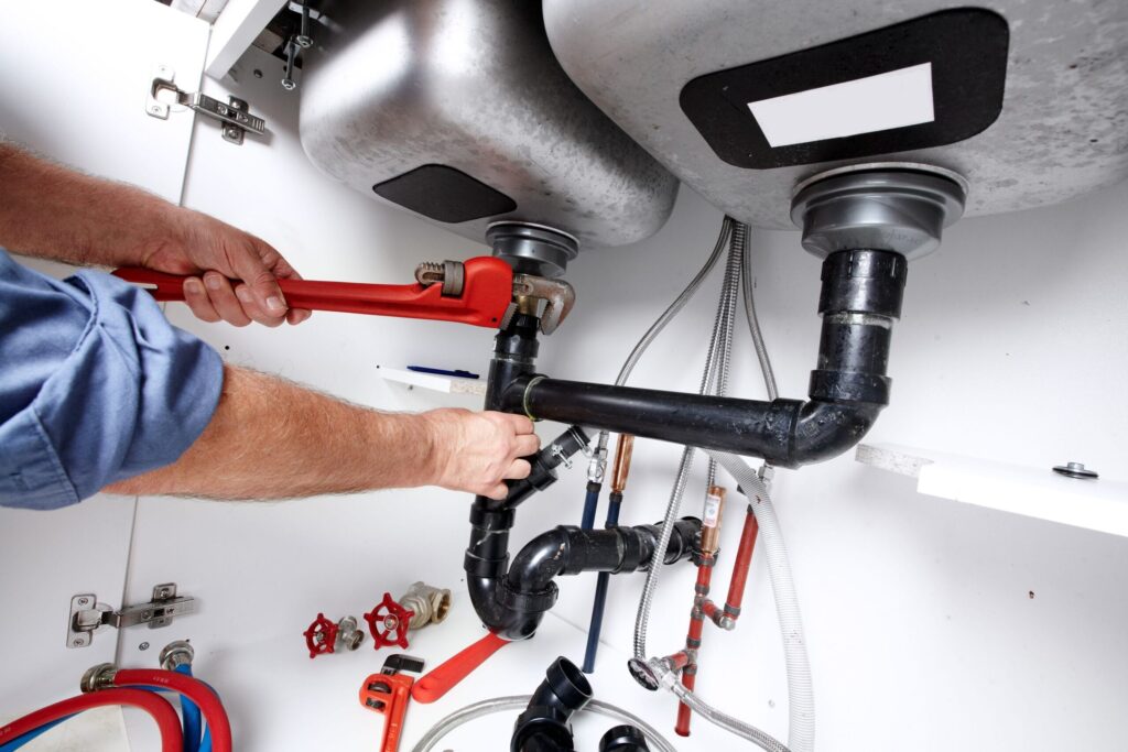 Plumber repairing drain pipes beneath a kitchen sink in Aurora
